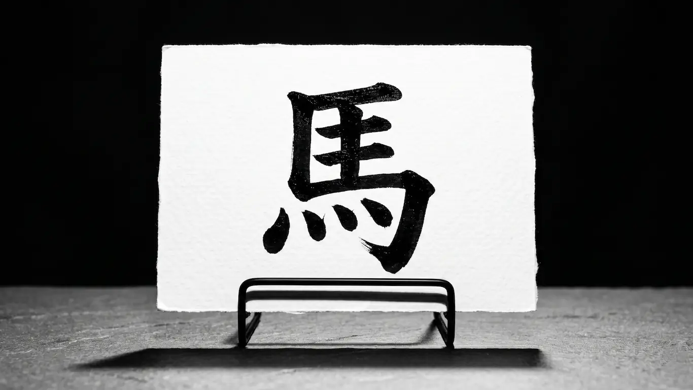 Plano medio de una tarjeta de alto contraste expuesta en un soporte, mostrando el kanji tradicional de caballo escrito con pincel