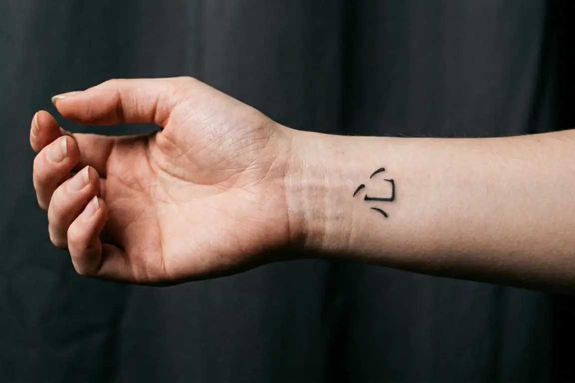 Plano medio de la muñeca de una mujer luciendo un tatuaje fino y realista del kanji de corazón Kokoro.
